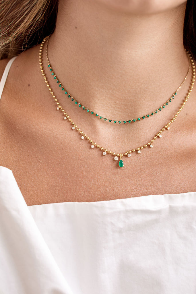 Layering de collares de oro y esmeraldas de ARA Joyería. Collar superior choker de pequeñas esmeraldas en forma de triángulo. Collar inferior de cuentas de oro y pequeños diamantes o circonitas, con un dije colgante de esmeralda en forma de lágrima. Collares apilables de oro para mujer.