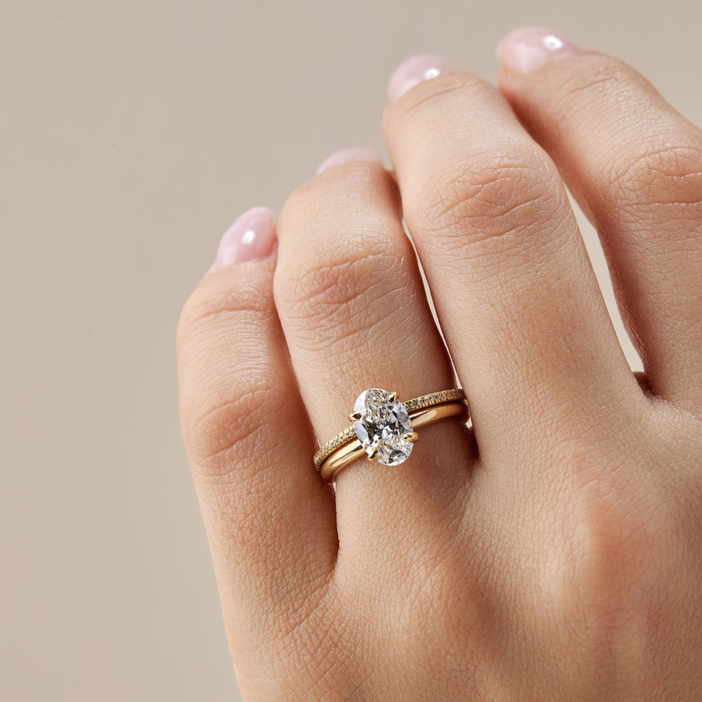 Anillo de compromiso de oro amarillo con solitario ovalado grande de diamante o moissanita. La pieza está combinada con una banda de matrimonio o churumbela fina con micropavé de diamantes en el dedo. Set de anillos apilables de pedida en oro para mujer.