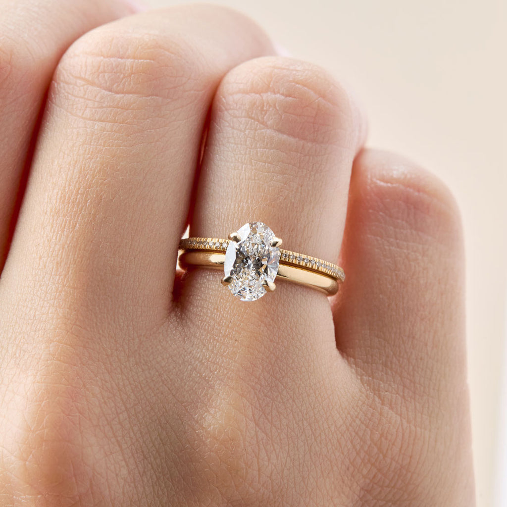 Anillo de compromiso de oro amarillo con un solitario ovalado que ilustra la alta claridad del diamante. La piedra central ovalada, de corte brillante, se muestra sin inclusiones visibles. El anillo de compromiso se combina con una banda de matrimonio o churumbela fina con micropavé. Anillo de pedida con diamante de claridad VVS o FL.