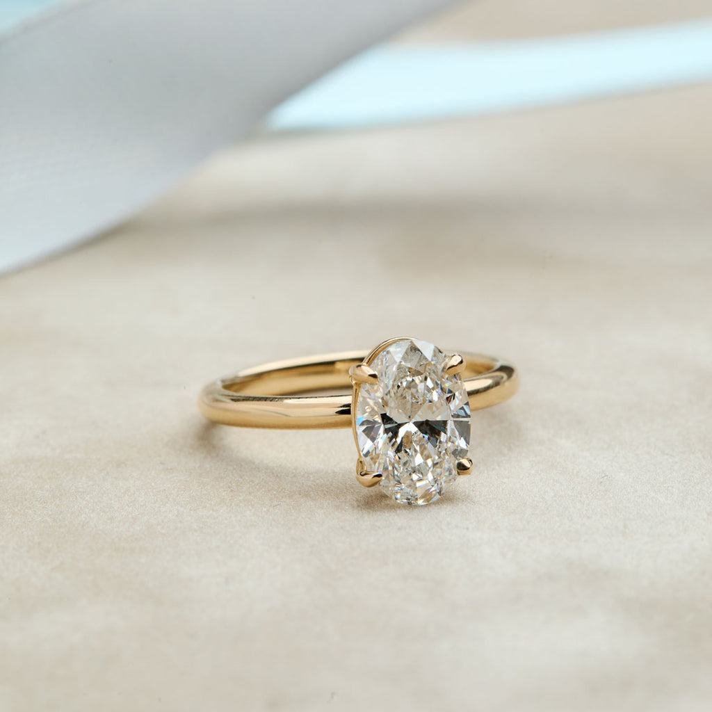 Anillo de compromiso de solitario ovalado de oro amarillo que ilustra el color de alta calidad del diamante (escala D-E-F). Primer plano de un diamante o moissanita con color incoloro o casi incoloro, sin tonos amarillentos. Anillo de pedida clásico y minimalista con diamante ovalado.