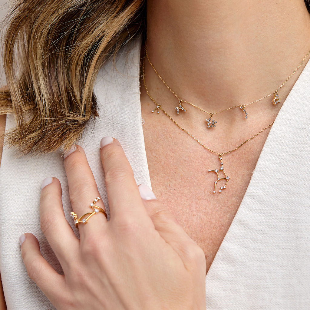 Joyería de constelaciones de la colección stARA de ARA Joyería. Primer plano de un collar choker de oro y un anillo de constelación con pequeños diamantes. La imagen muestra dos collares: un choker con pequeñas estrellas de zodiaco y un collar largo con un dije grande de constelación. Anillo de oro y estrellas para mujer.